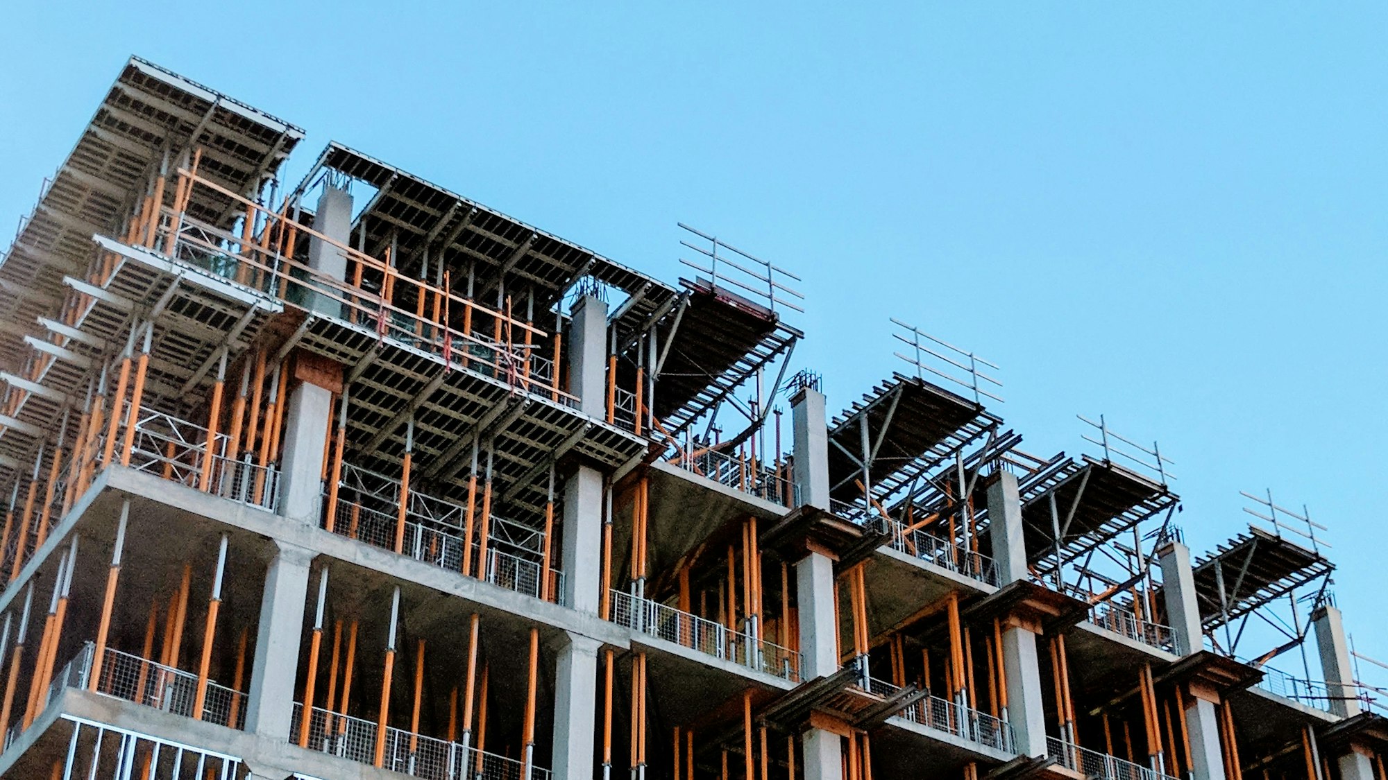 Struttura in cemento armato di un edificio in costruzione con casseri e puntelli, contro il cielo azzurro